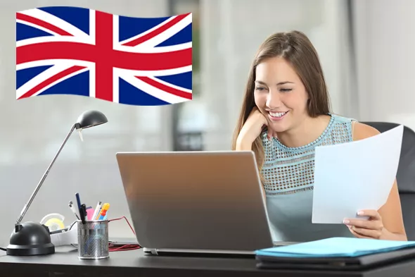 Mujer sonriente trabajando en una computadora portátil con documentos en la mano, mientras se muestra la bandera del Reino Unido en el fondo.