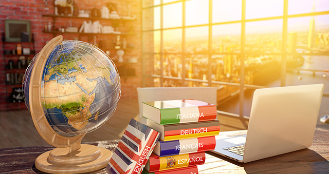 Imagen de un escritorio con un globo terráqueo y una pila de libros de idiomas, incluyendo inglés, español, francés, alemán e italiano, junto a una laptop. La luz del sol entra por una ventana grande, creando un ambiente cálido y acogedor. Ideal para temas de aprendizaje de idiomas y educación.