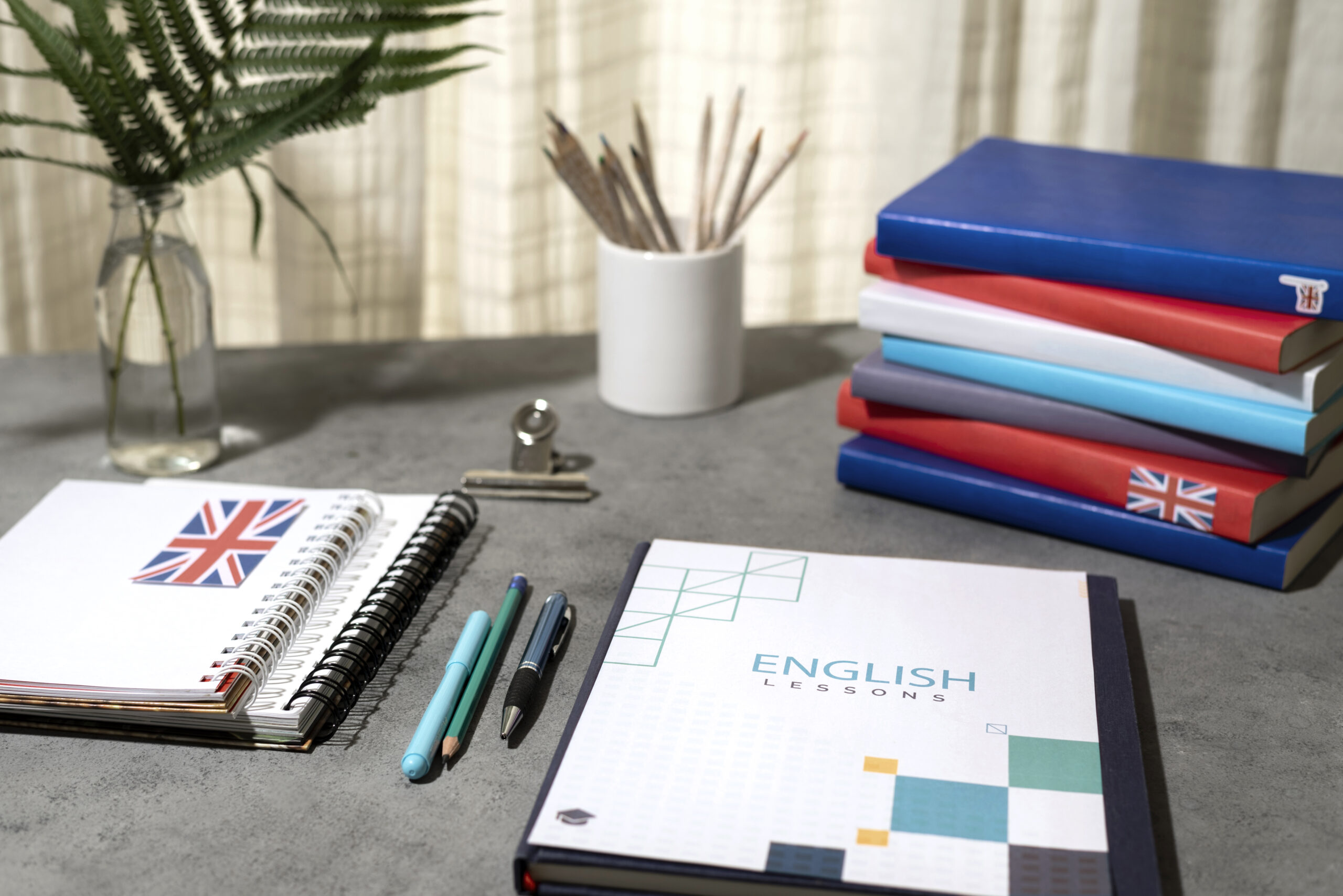 Escritorio organizado con materiales de estudio para lecciones de inglés, incluyendo cuadernos, bolígrafos y un libro titulado "ENGLISH LESSONS", decorado con banderas británicas.