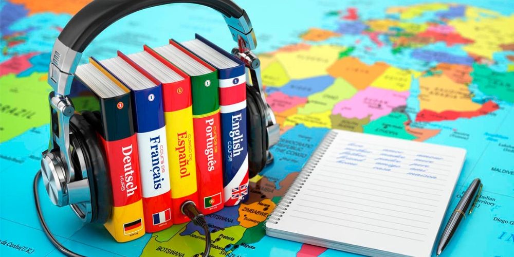 Auriculares sobre libros de idiomas, incluyendo español, francés, alemán y portugués, junto a un cuaderno y un mapa del mundo, ideal para el aprendizaje de idiomas.